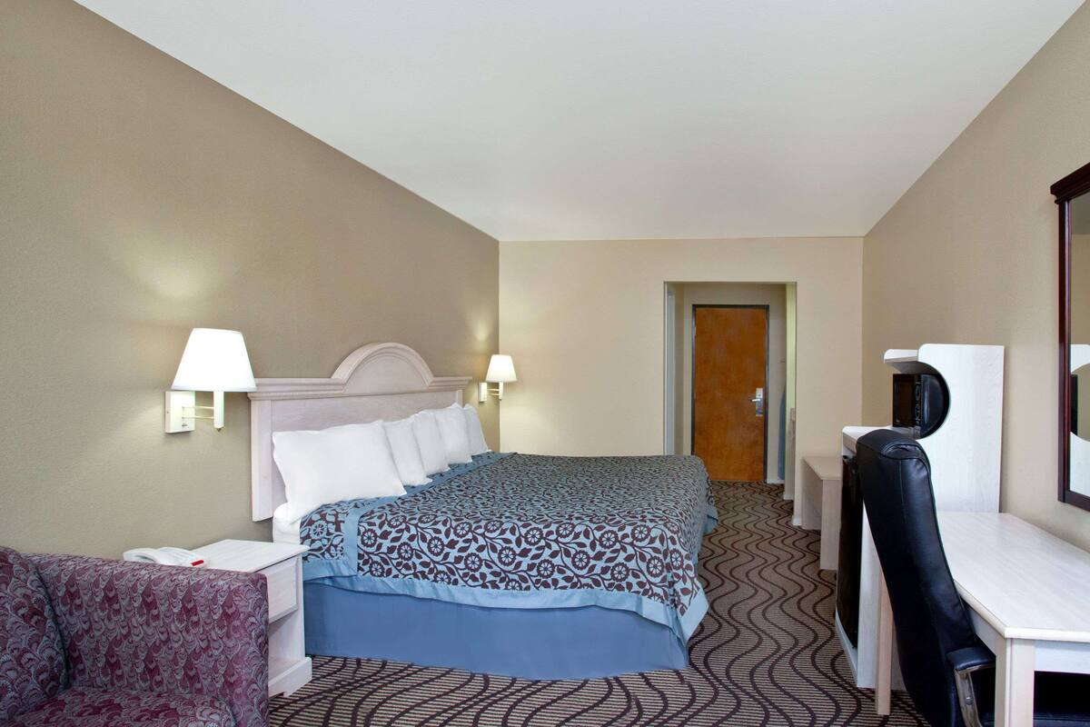 Ein Hotelzimmer mit einem Bett, Nachttischlampen, einem Schreibtisch mit Stuhl und einem Fernseher.