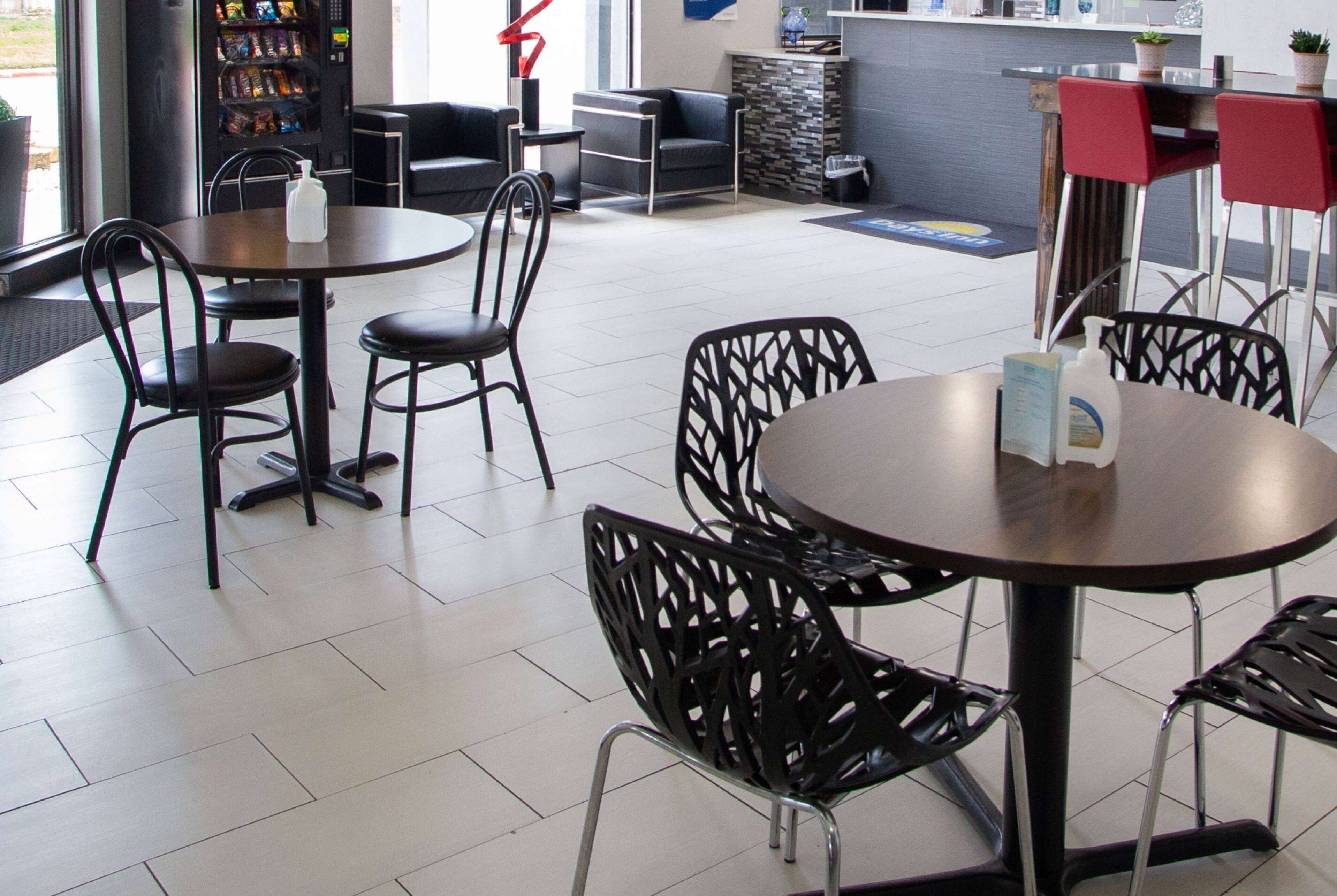 Restaurante moderno com mesas redondas e cadeiras pretas, uma máquina de vendas automática e um balcão com uma planta.