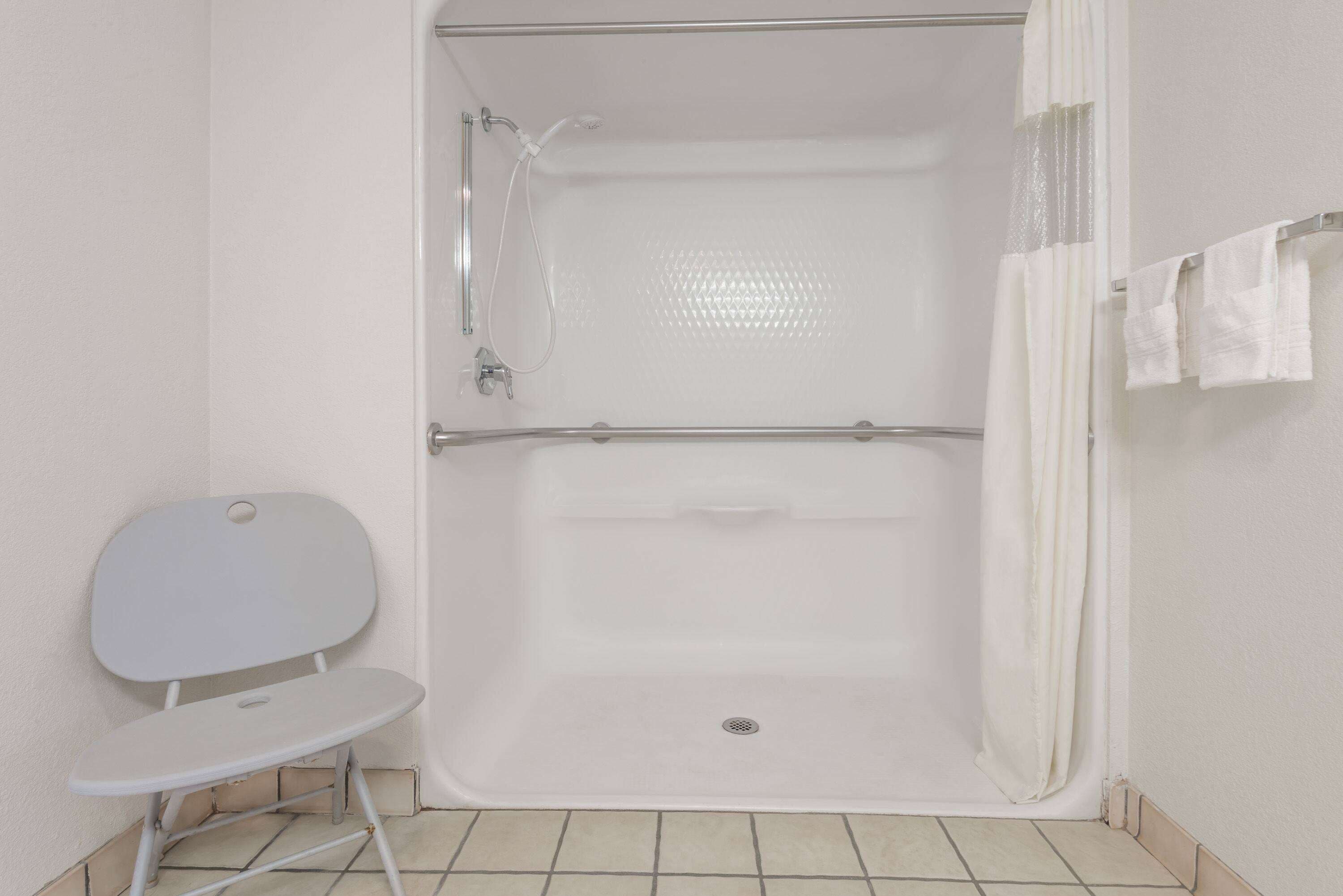 A shower with a grab bar, a small step stool, and a towel rack.