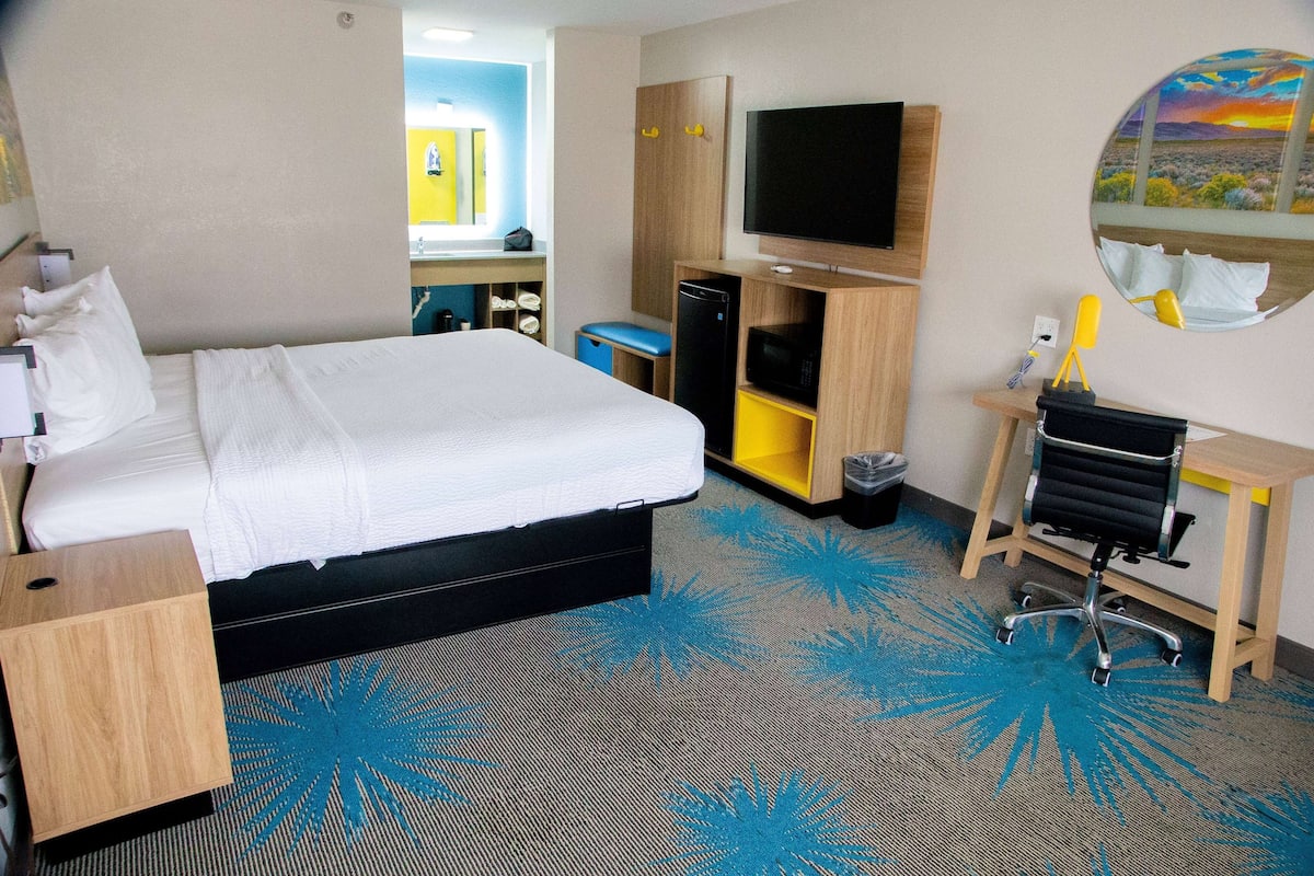 Une chambre d’hôtel avec un lit, un bureau, une télévision et une salle de bain visible à travers une porte ouverte.