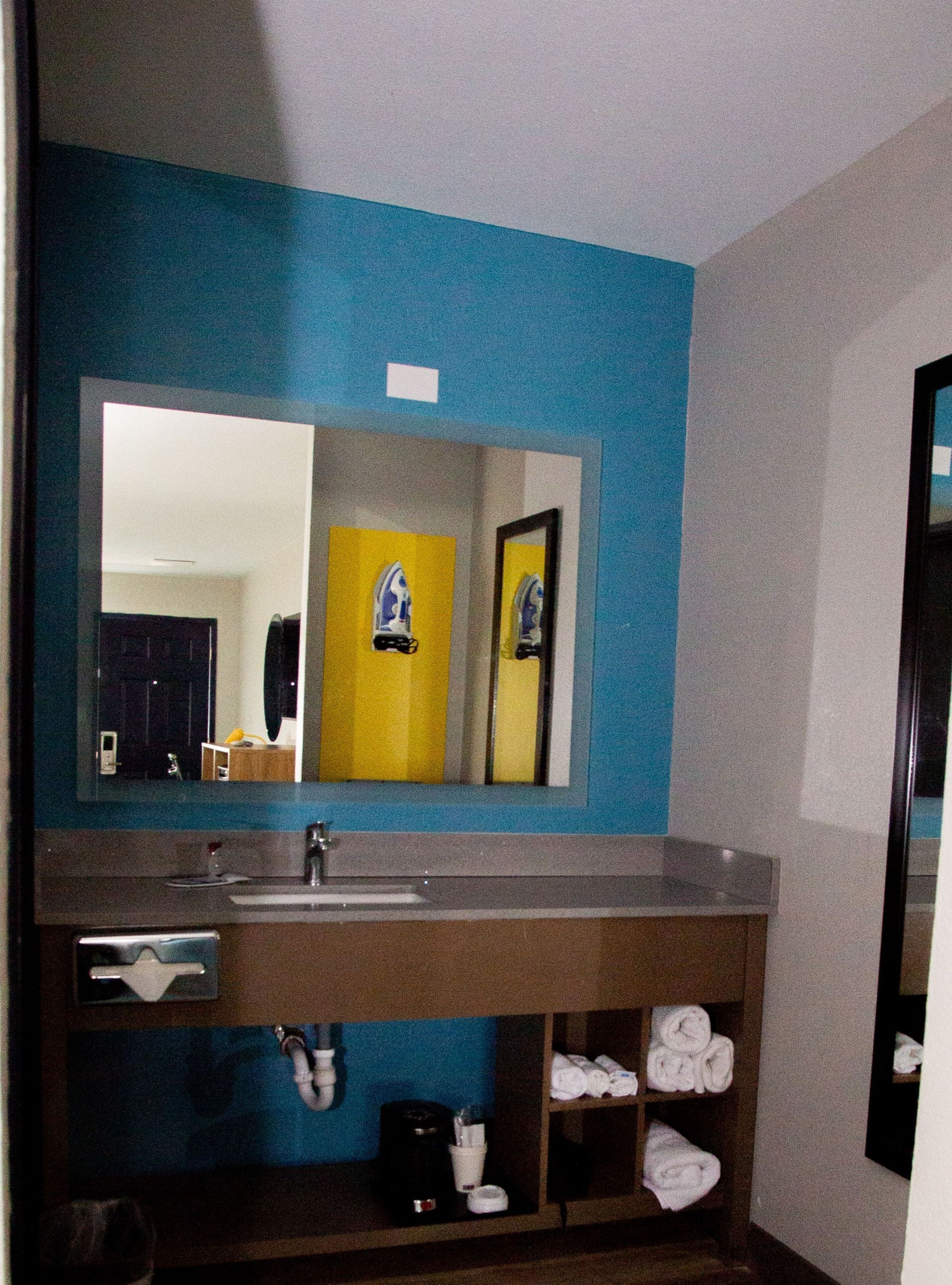 Une salle de bain avec un mur bleu, un grand miroir, un lavabo et un porte-serviettes.