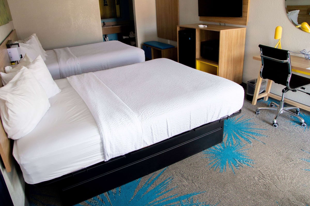 Une chambre d’hôtel avec deux lits, un bureau, une chaise, une télévision et une poubelle.