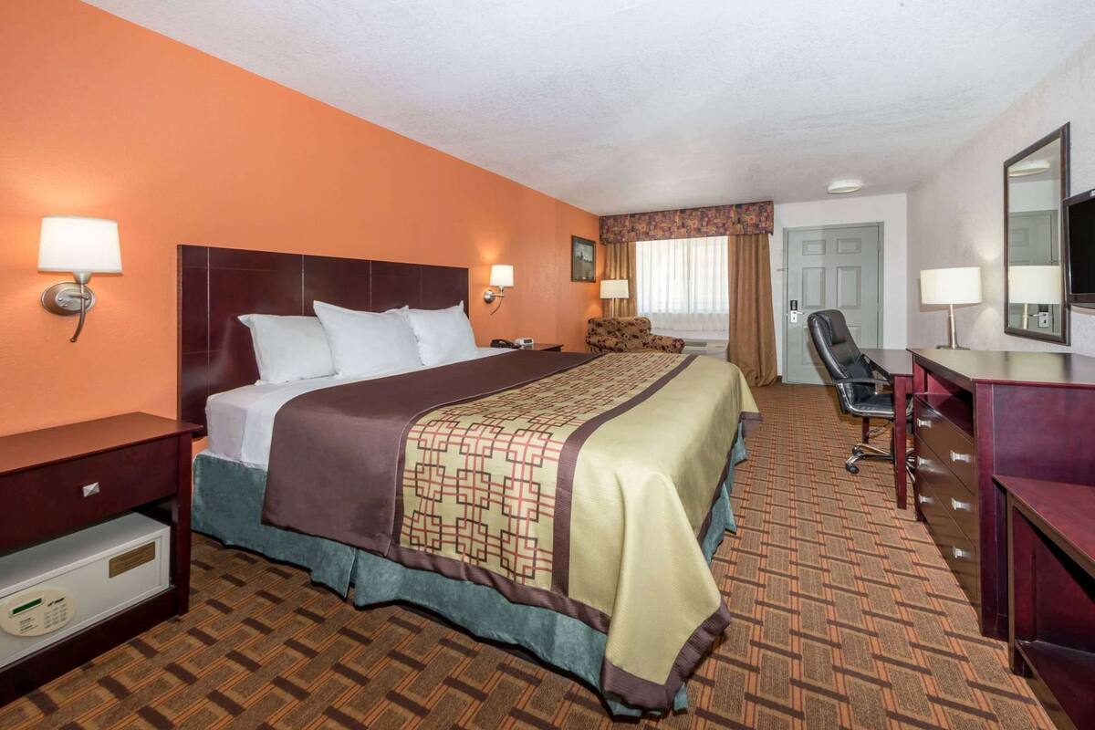 A hotel room with a bed, a desk, a chair, a dresser, and a television.