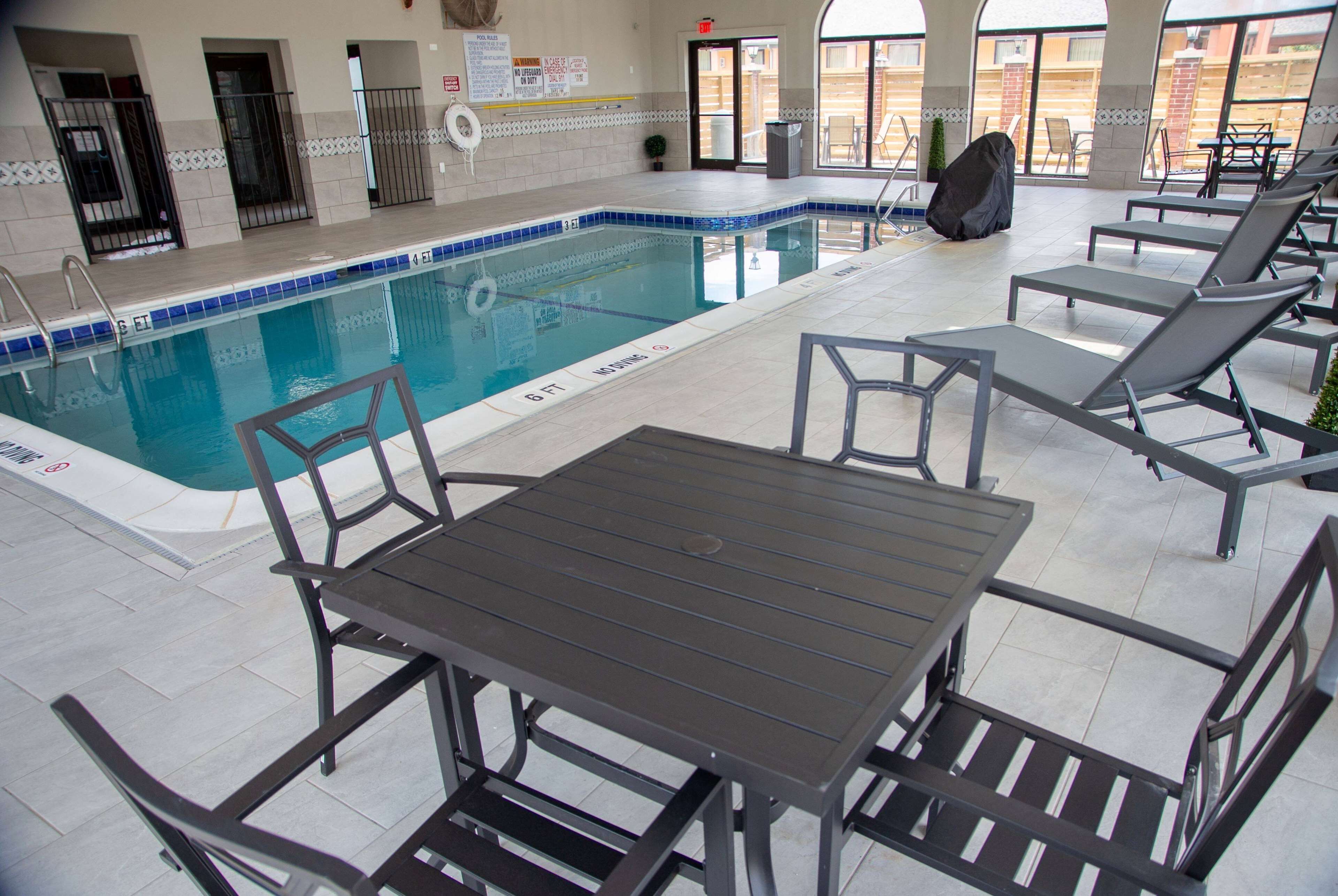 Un área de piscina con una piscina con baldosas, sillas de descanso y una mesa.