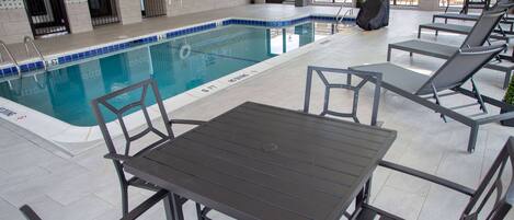 Un área de piscina con una piscina con baldosas, sillas de descanso y una mesa.