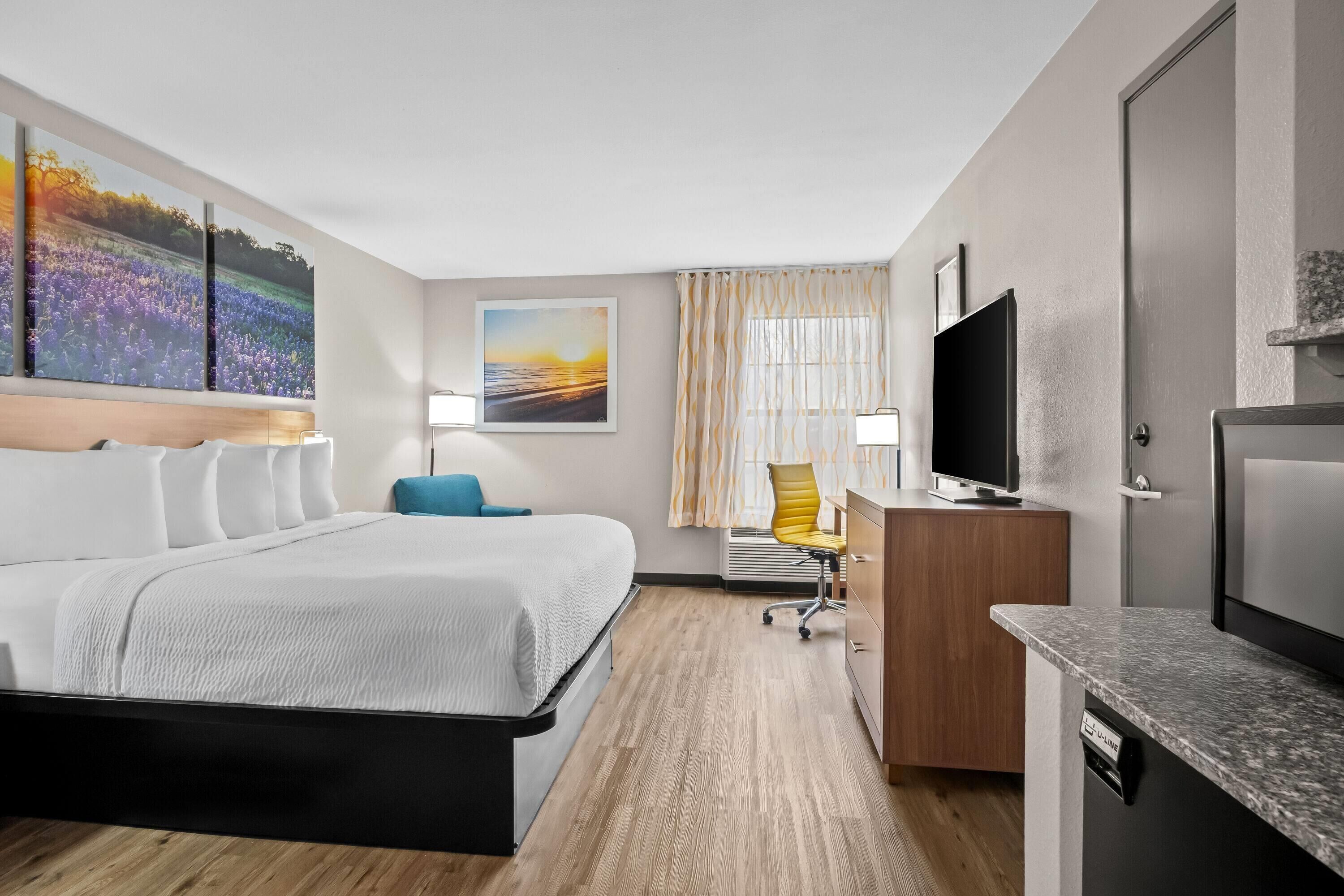 A hotel room with a bed, desk, television, and artwork on the walls.