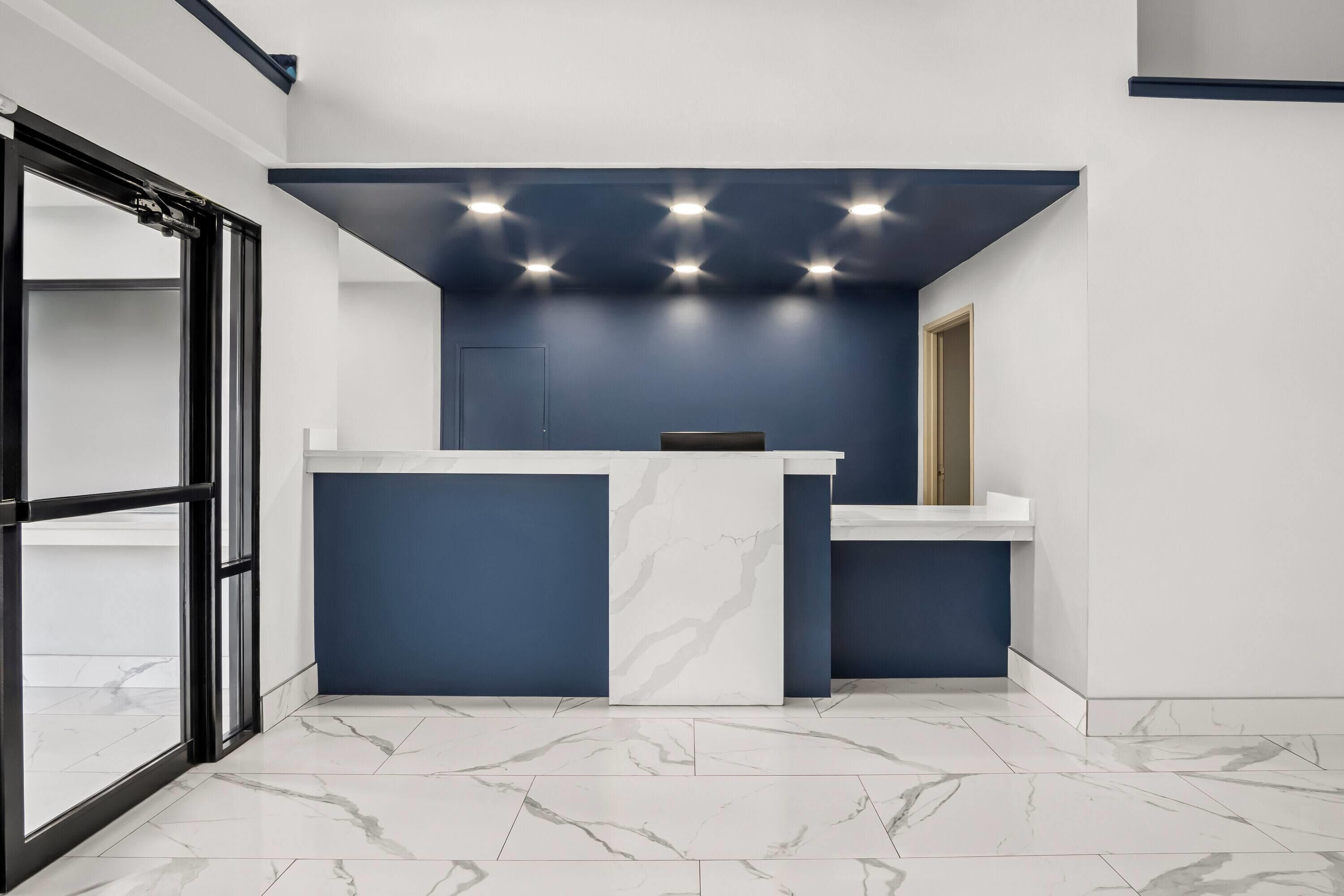 A reception desk with a marble countertop, a blue accent wall, and a ceiling with recessed lighting.
