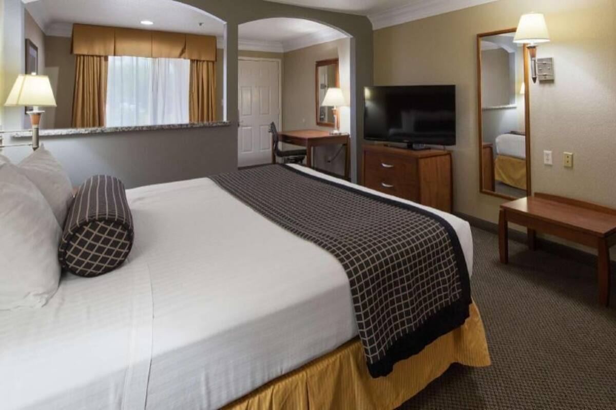 Quarto de hotel com cama grande, escrivaninha, televisão e espelho.