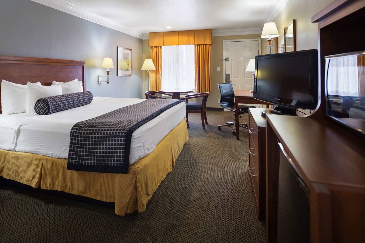Quarto de hotel com uma cama grande, uma mesa com televisão e uma cadeira.