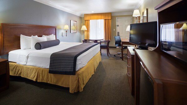 A hotel room with a large bed, a desk with a television, and a chair.