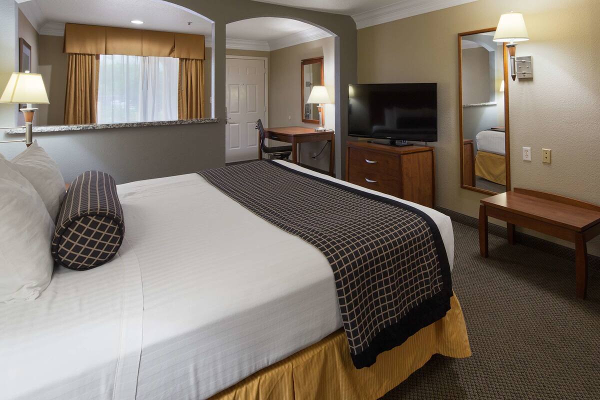 Quarto de hotel com uma cama grande, uma escrivaninha, uma televisão e um espelho.