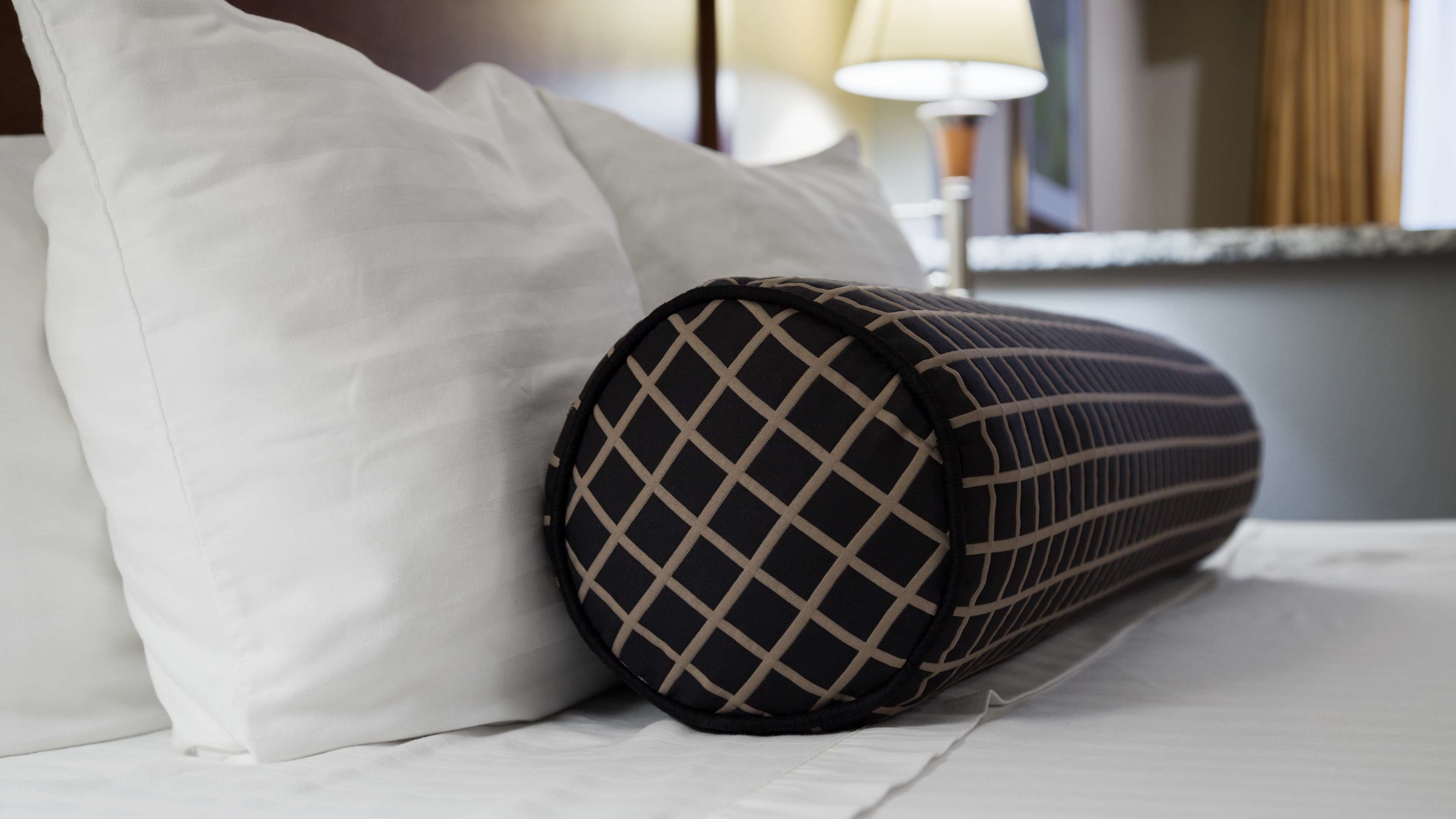 A bed with white bedding and a black and beige pillow.