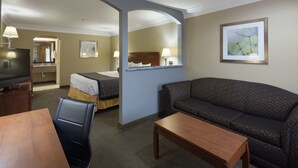 Habitación de hotel con cama, sofá, televisión, escritorio y baño visible a través de un arco.