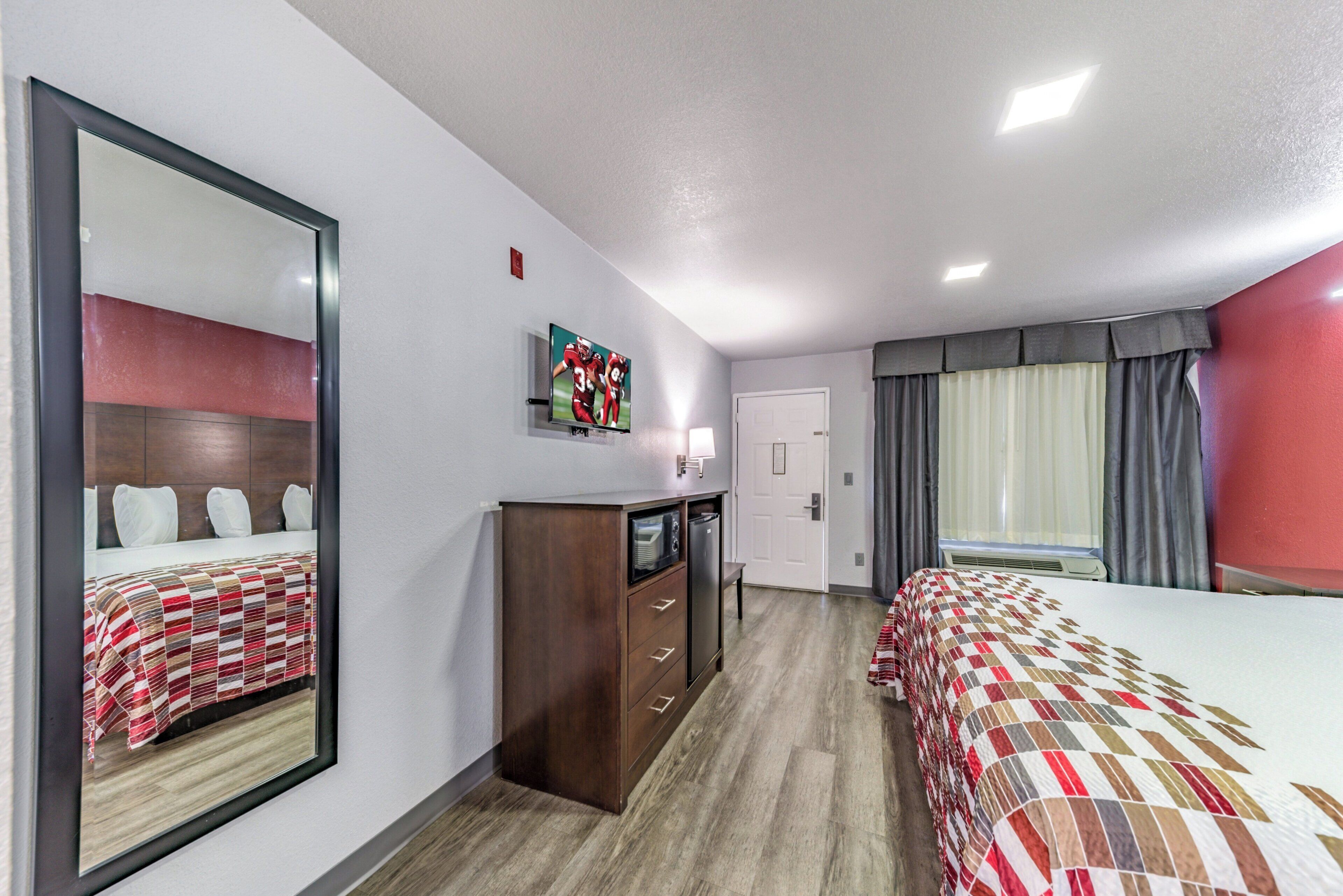 A hotel room with two beds, a TV, a dresser, and a window with curtains.