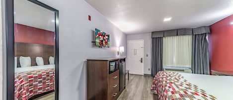A hotel room with two beds, a TV, a dresser, and a window with curtains.