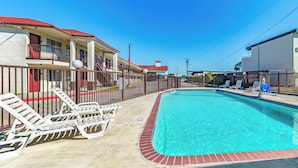 A swimming pool with lounge chairs, a fenced area, and a building with a red roof. - Red Roof Inn Dallas - Mesquite/ Fair Park NE (Mesquite)