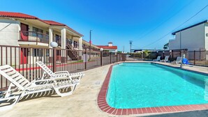 A swimming pool with lounge chairs, a fenced area, and a building with a red roof. - Red Roof Inn Dallas - Mesquite/ Fair Park NE (Mesquite)