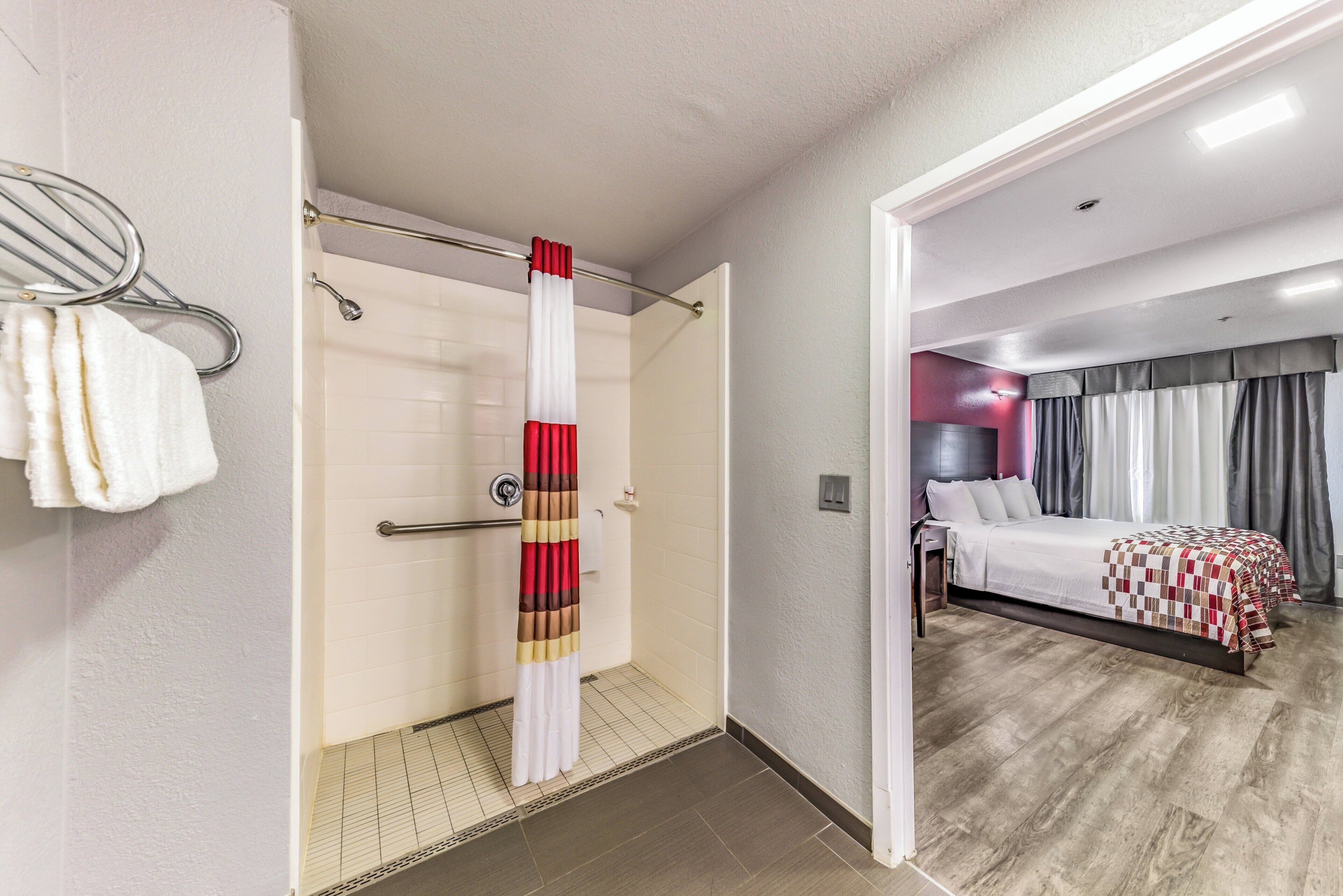 Habitación de hotel con ducha, cama y baño con toallero.