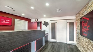 A hotel reception area with a Red Roof Inn sign, a clock, and a sign indicating free Wi-Fi in all rooms. - Red Roof Inn Dallas - Mesquite/ Fair Park NE (Mesquite)