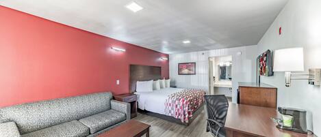 A hotel room with a bed, a sofa, a desk, and a chair.