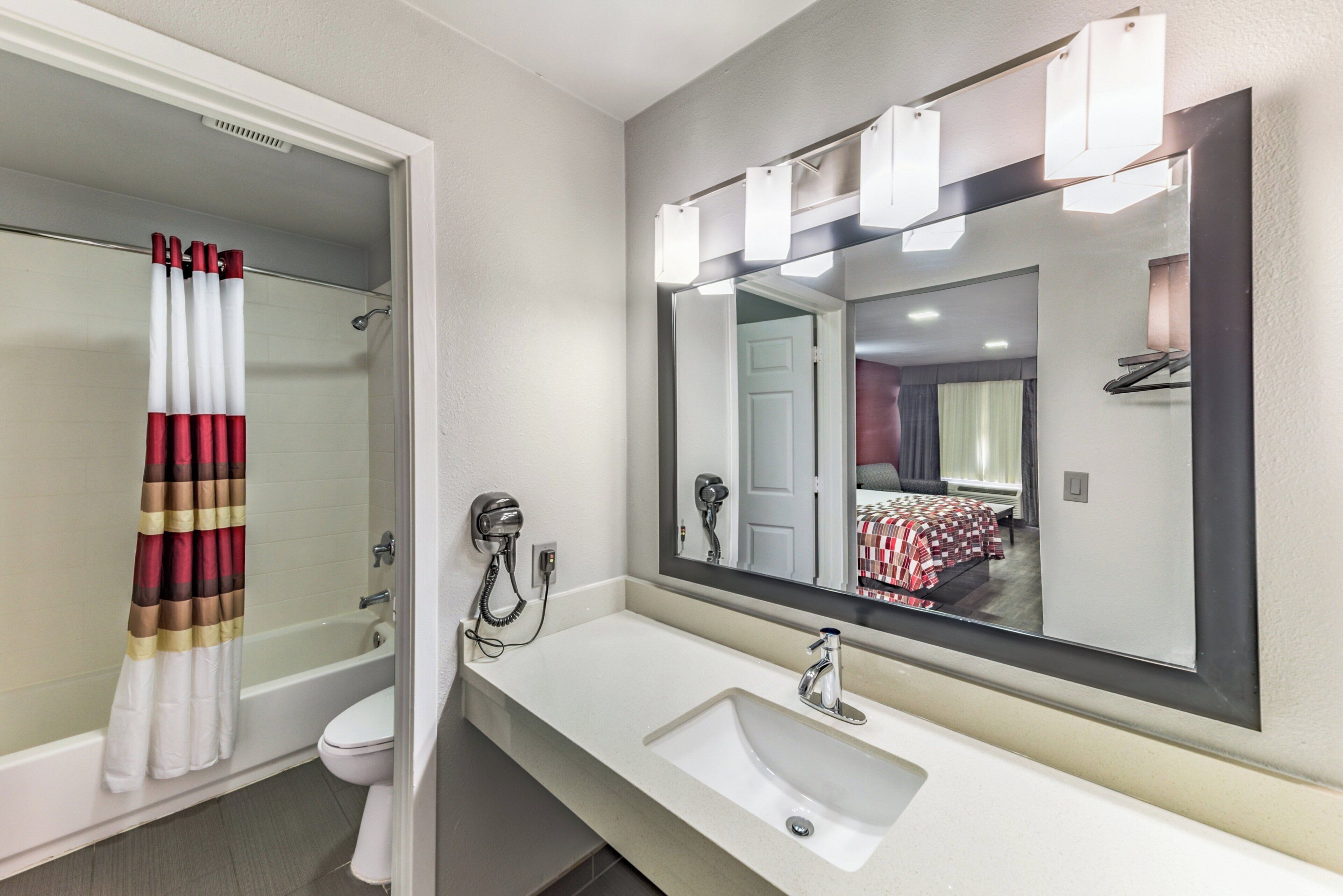 A bathroom with a shower, toilet, sink, and a large mirror.