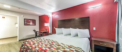 A hotel room with a bed, a desk, a chair, and a nightstand.