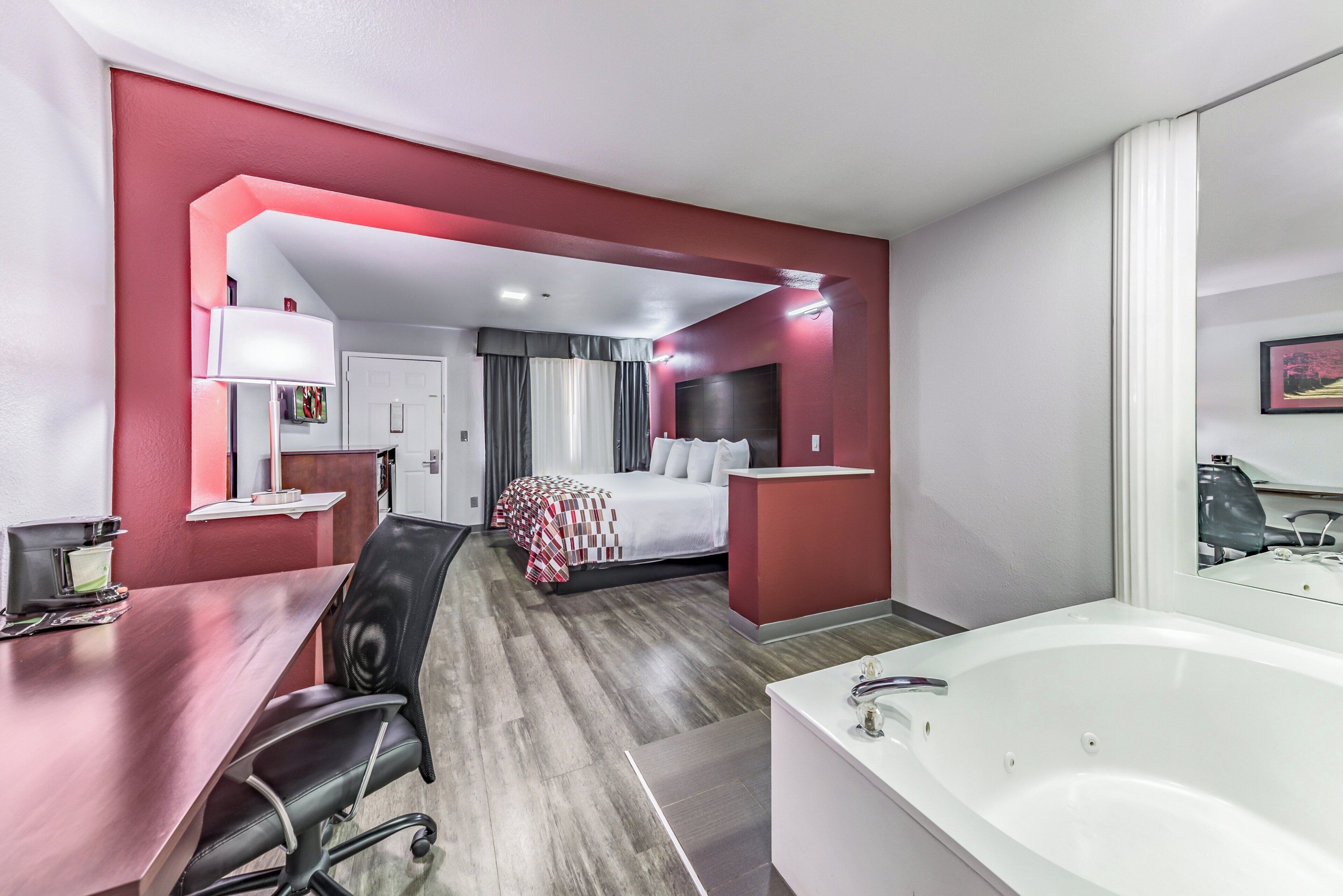A hotel room with a bed, a desk with a chair, a bathroom with a bathtub, and a mirror.
