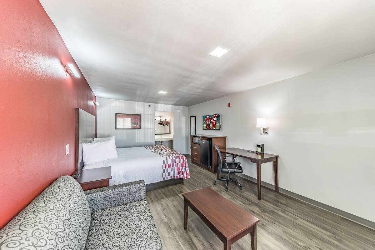 A hotel room with a bed, a desk, a chair, a sofa, and a small table.