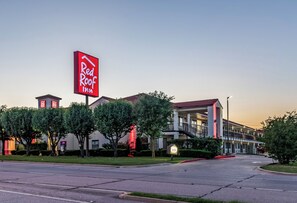 A Red Roof Inn with a large red sign, a parking lot, and a building with a red roof. - Red Roof Inn Dallas - Mesquite/ Fair Park NE (Mesquite)