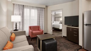 A hotel room with a sofa, armchair, TV, and a small table. - Homewood Suites by Hilton North Dallas-Plano (Plano)