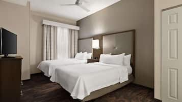 Habitación de hotel con dos camas, televisión, ventilador de techo y un ventanal grande con cortinas.