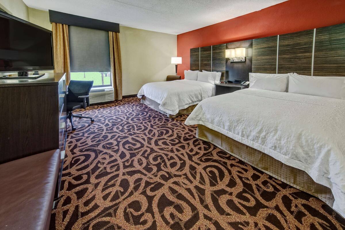 A hotel room with two beds, a desk with a TV, a lamp, and a patterned carpet.