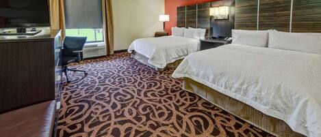 Habitación de hotel con dos camas, un escritorio con televisor, una lámpara y una alfombra estampada.