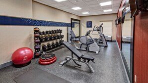 Une salle de sport équipée de matériel d’exercice, notamment des haltères, un ballon d’exercice rouge et un banc.