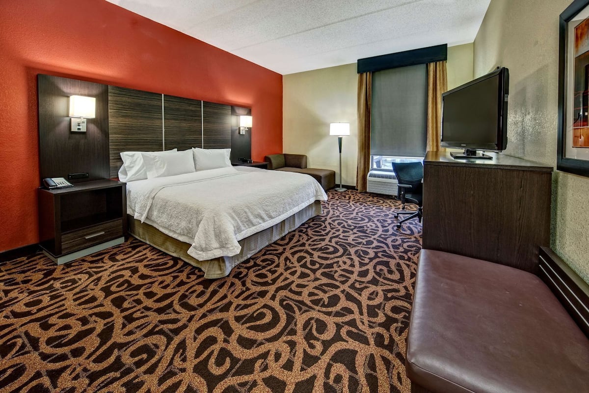 A hotel room with a bed, a desk, a chair, a TV, and a patterned carpet.