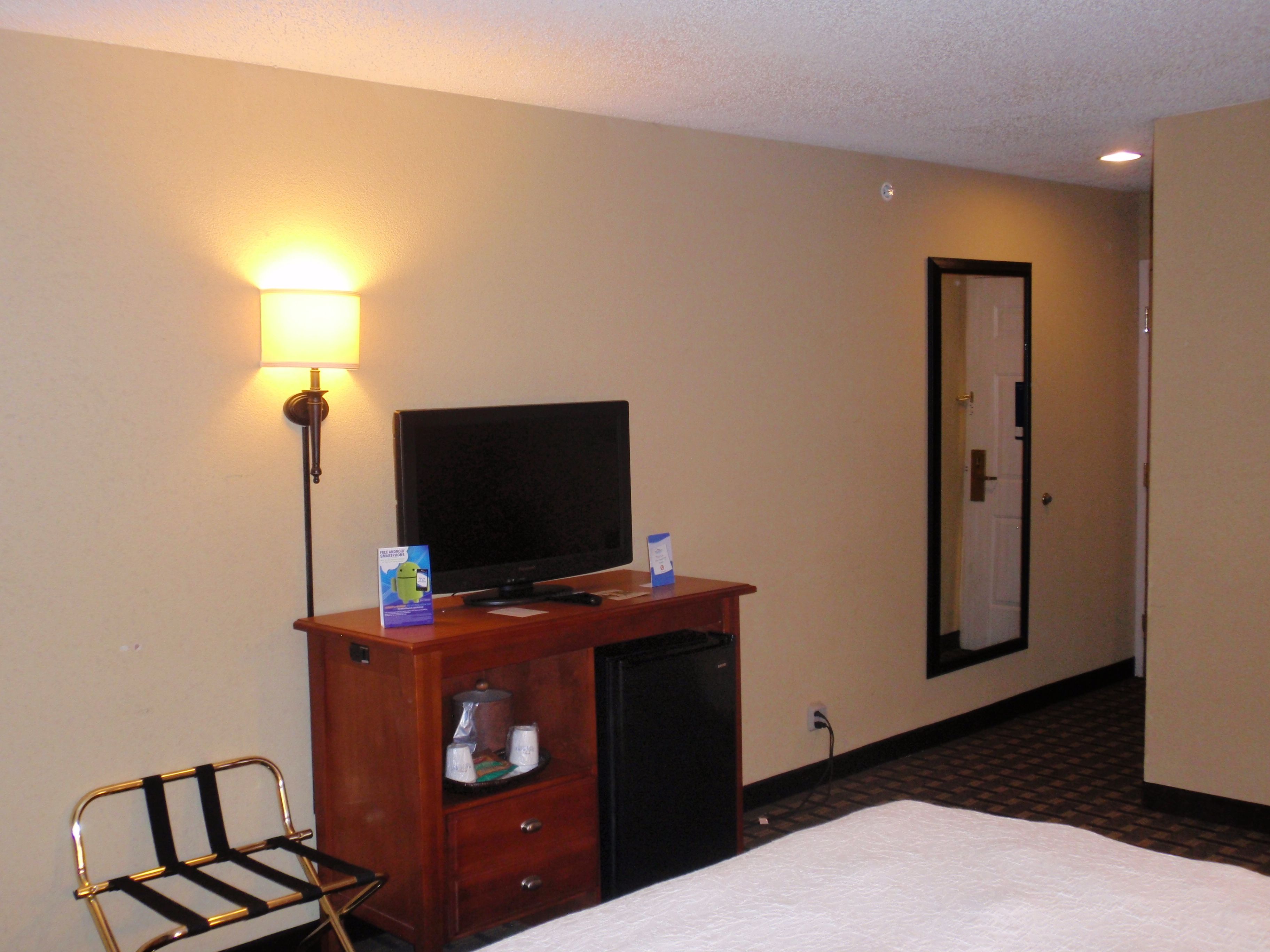 A hotel room with a bed, a desk with a television, a lamp, and a chair.