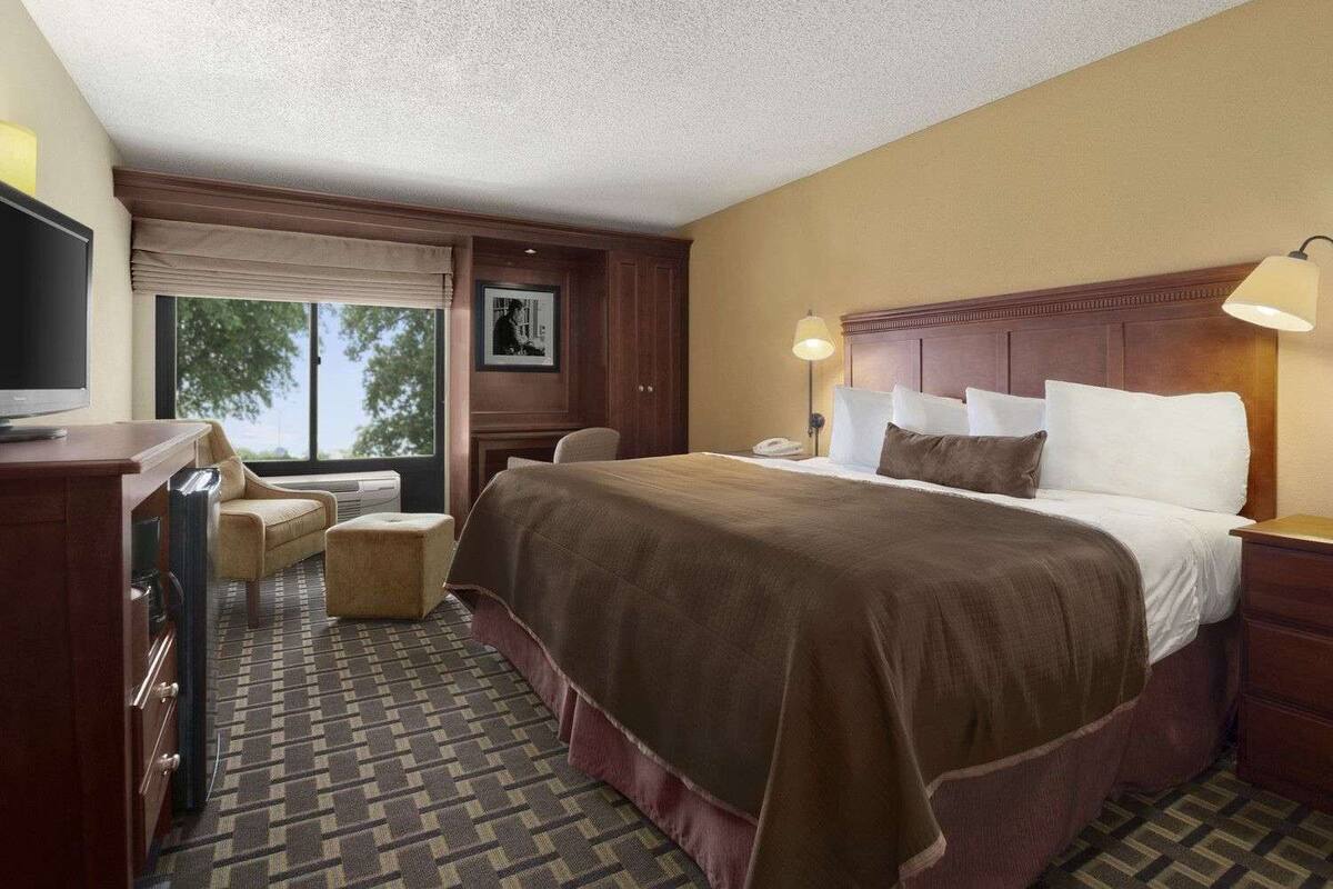 Une chambre d’hôtel avec un grand lit, un bureau avec une télévision, une chaise, une fenêtre donnant sur un beau paysage et un tableau encadré au mur.