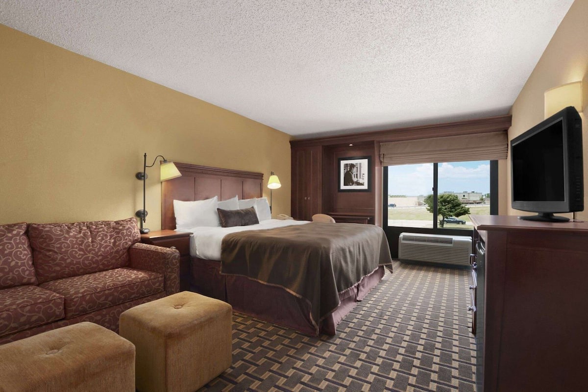 Une chambre d’hôtel avec un lit, un canapé, une télévision et une fenêtre donnant sur un paysage agréable.