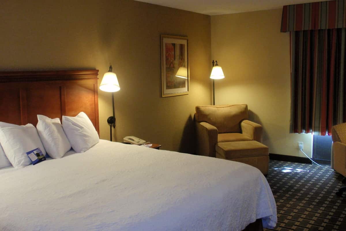 Une chambre d’hôtel avec un grand lit, deux lampes de chevet, une chaise, un téléphone et un tableau au mur.