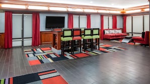 A modern hotel room with a large flat-screen TV, a dining area with chairs and a table, a sofa, and a patterned rug. - Days Inn & Suites by Wyndham Tyler (Tyler)