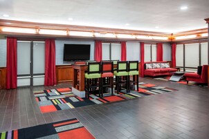 Una habitación de hotel moderna con un televisor de pantalla plana grande, un rincón de comedor con sillas y una mesa, un sofá y una alfombra estampada.