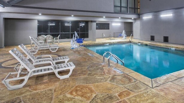 An indoor swimming pool with clear water, surrounded by stone tiles and equipped with multiple lounge chairs and a diving board. - Days Inn & Suites by Wyndham Tyler (Tyler)