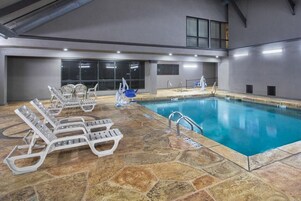 Piscina interior con agua cristalina, rodeada de baldosas de piedra y equipada con numerosas tumbonas y un trampolín.