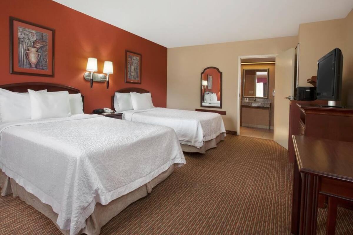A hotel room with two beds, a television, a desk, and a mirror.