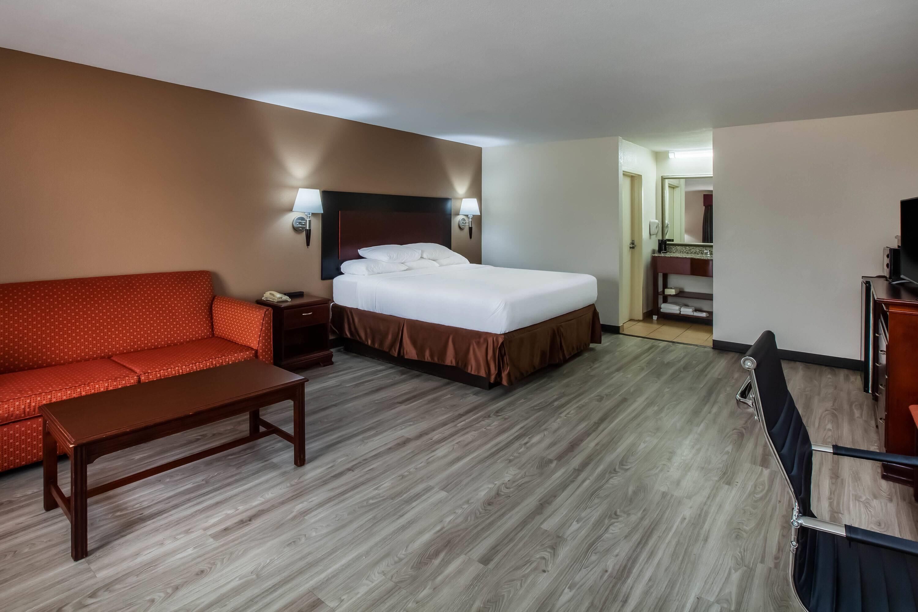 A hotel room with a bed, a sofa, a desk, and a TV.
