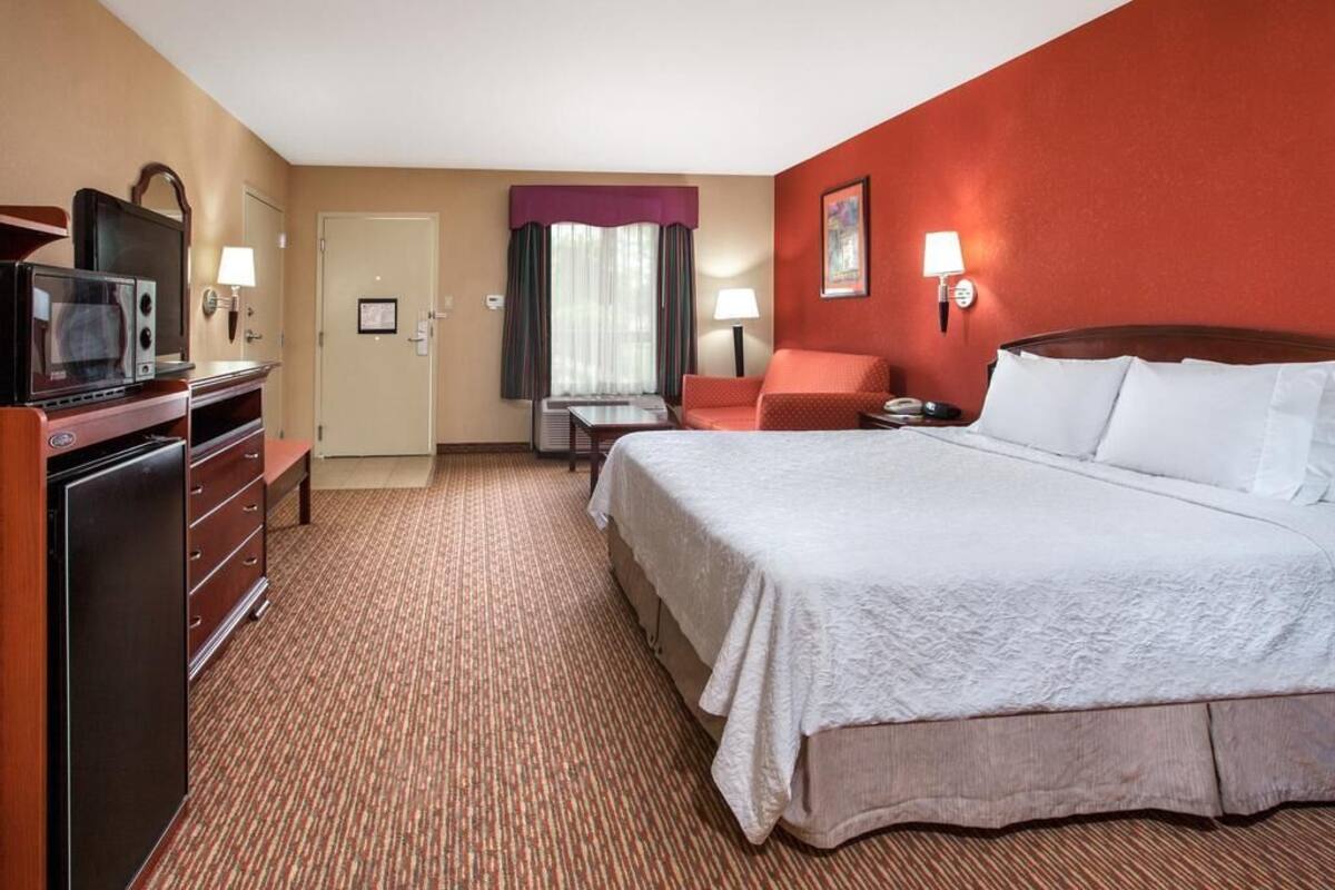 A hotel room with a large bed, a desk with a chair, a television, and a dresser.