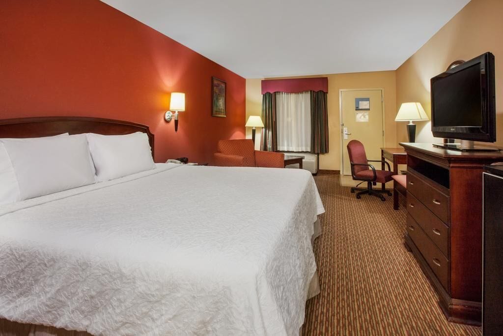 A hotel room with a large bed, a desk with a chair, a television, and a dresser.