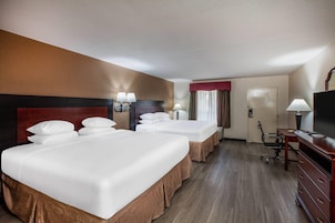 Habitación de hotel con tres camas, un escritorio, televisor y una silla.
