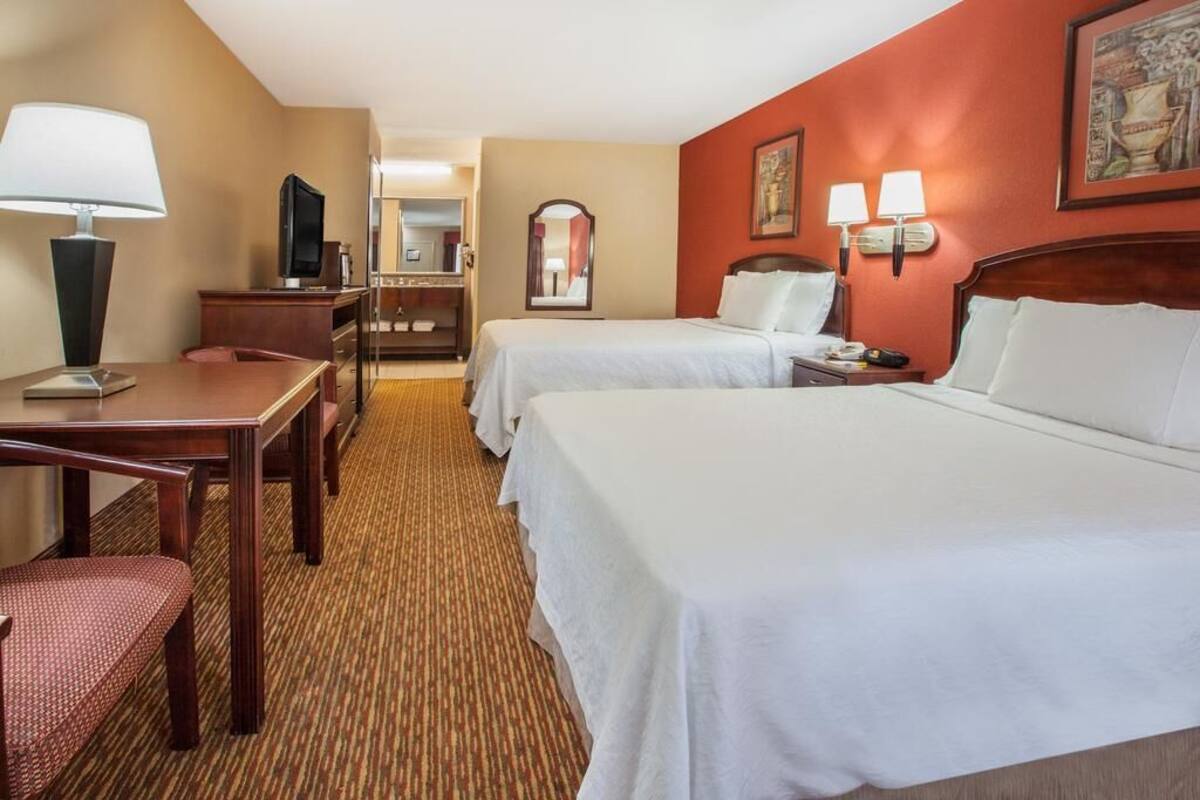 A hotel room with two beds, a desk, a chair, a television, and a mirror.