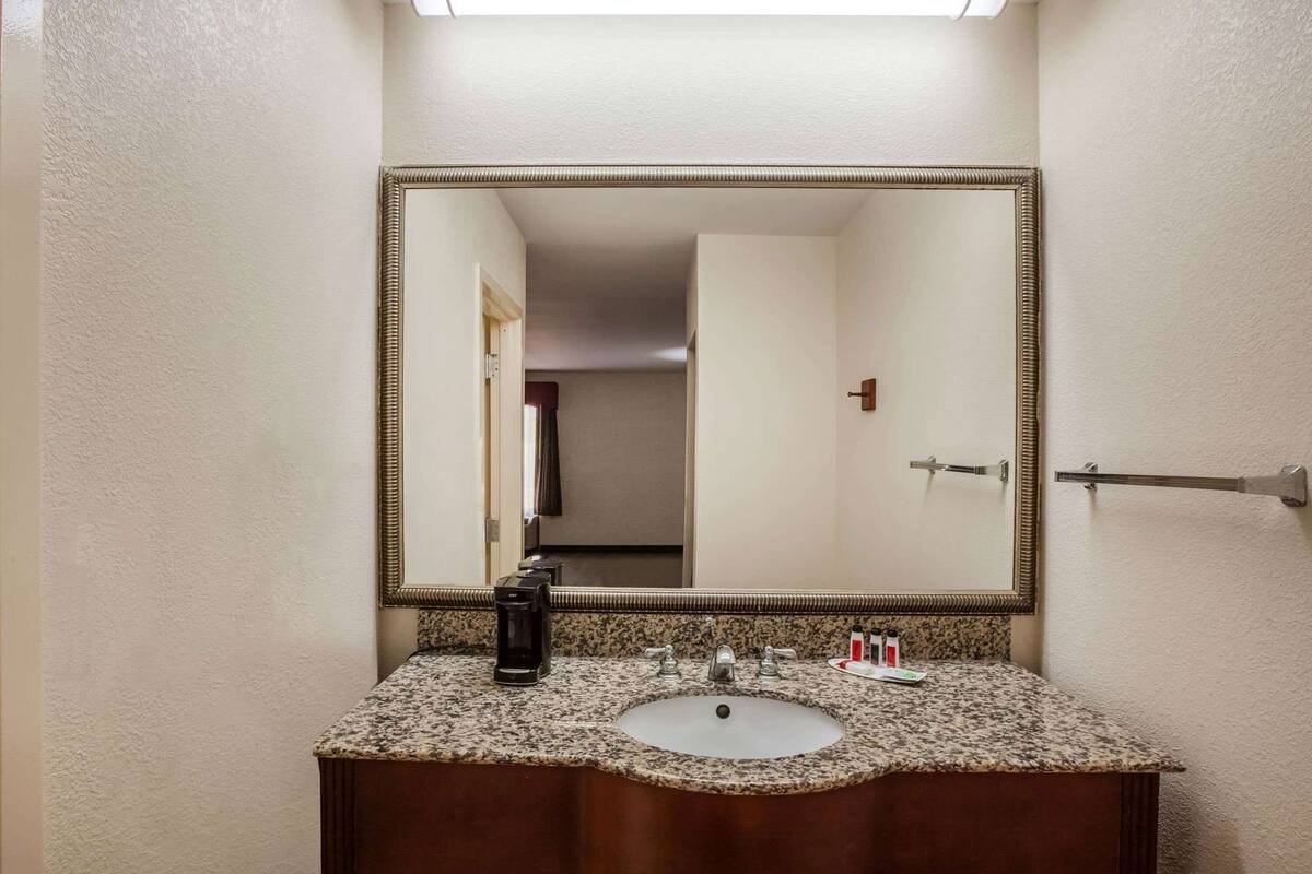 A bathroom with a granite countertop sink, a large mirror, and a towel rack.